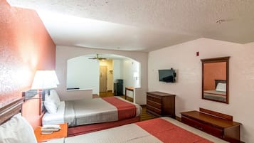 Habitación de hotel con cama, mesita de noche, lámpara, cómoda, espejo y televisor en la pared.