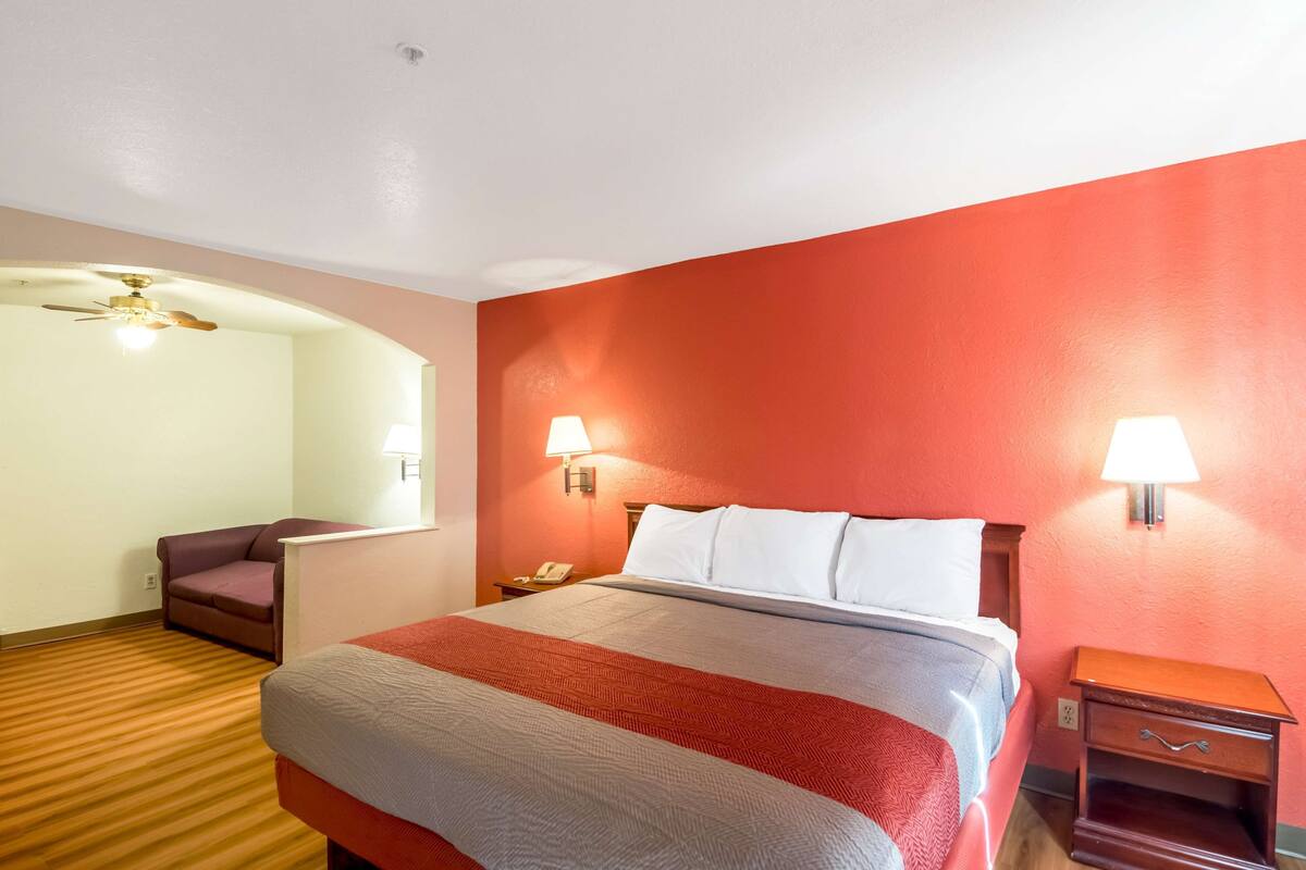 Ett hotellrum med en säng, två sänglampor, ett nattduksbord, en stol och en takfläkt.