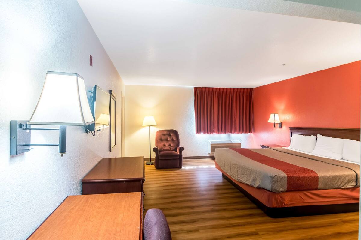 Ett hotellrum med en säng, ett skrivbord, en stol, en lampa och ett fönster med gardiner.