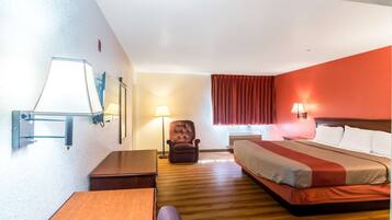 A hotel room with a bed, a desk, a chair, a lamp, and a window with curtains.
