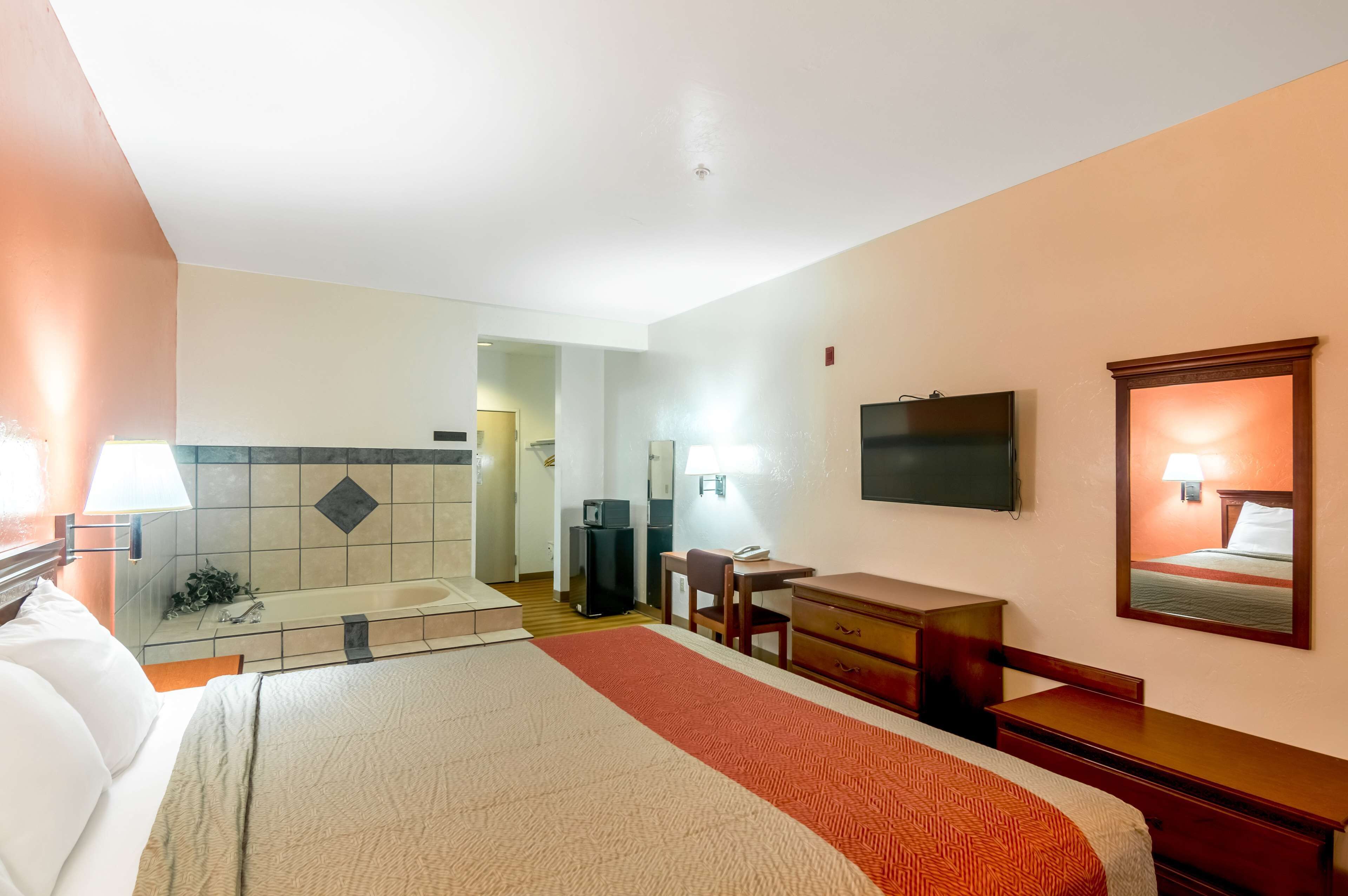 Une chambre d’hôtel avec un lit, un bureau, une chaise, une télévision et une salle de bain visible au fond.