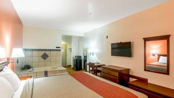 Une chambre d’hôtel avec un lit, un bureau, une chaise, une télévision et une salle de bain visible au fond.