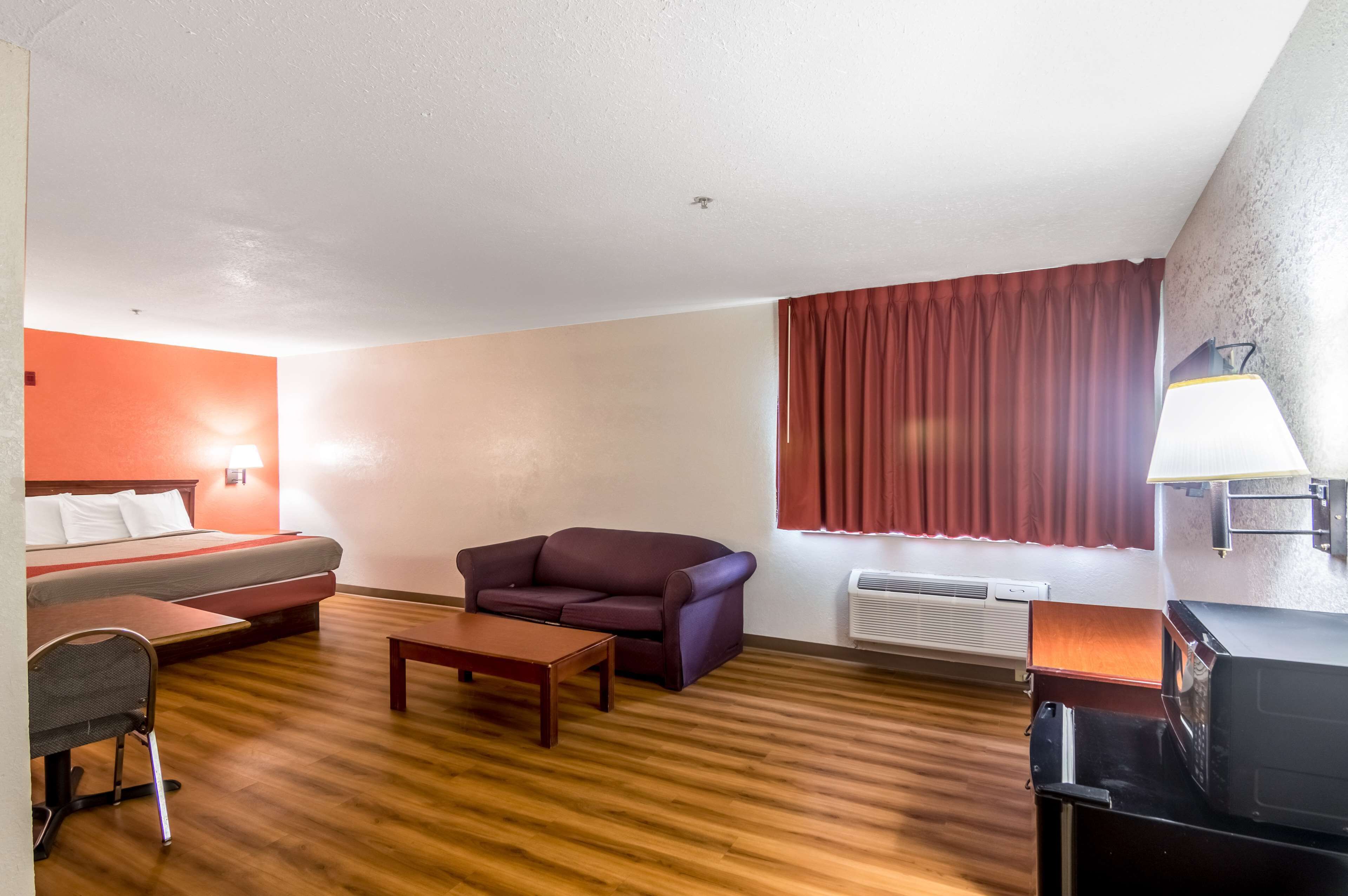 Een kamer met een bed, een bank, een stoel, een tafel, een lamp en een magnetron.