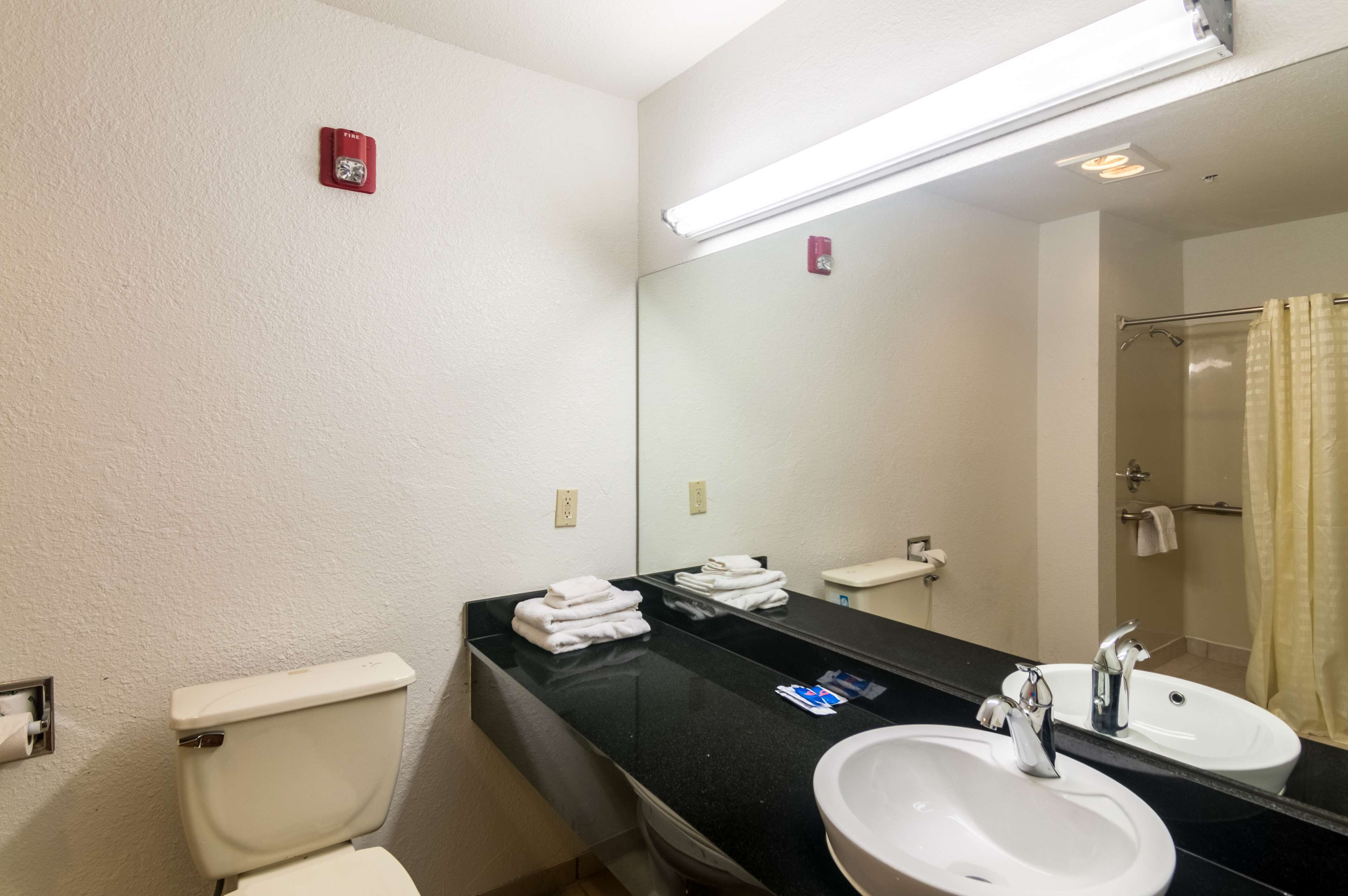 A bathroom with a toilet, sink, and mirror. There are towels on the counter and a shower curtain.
