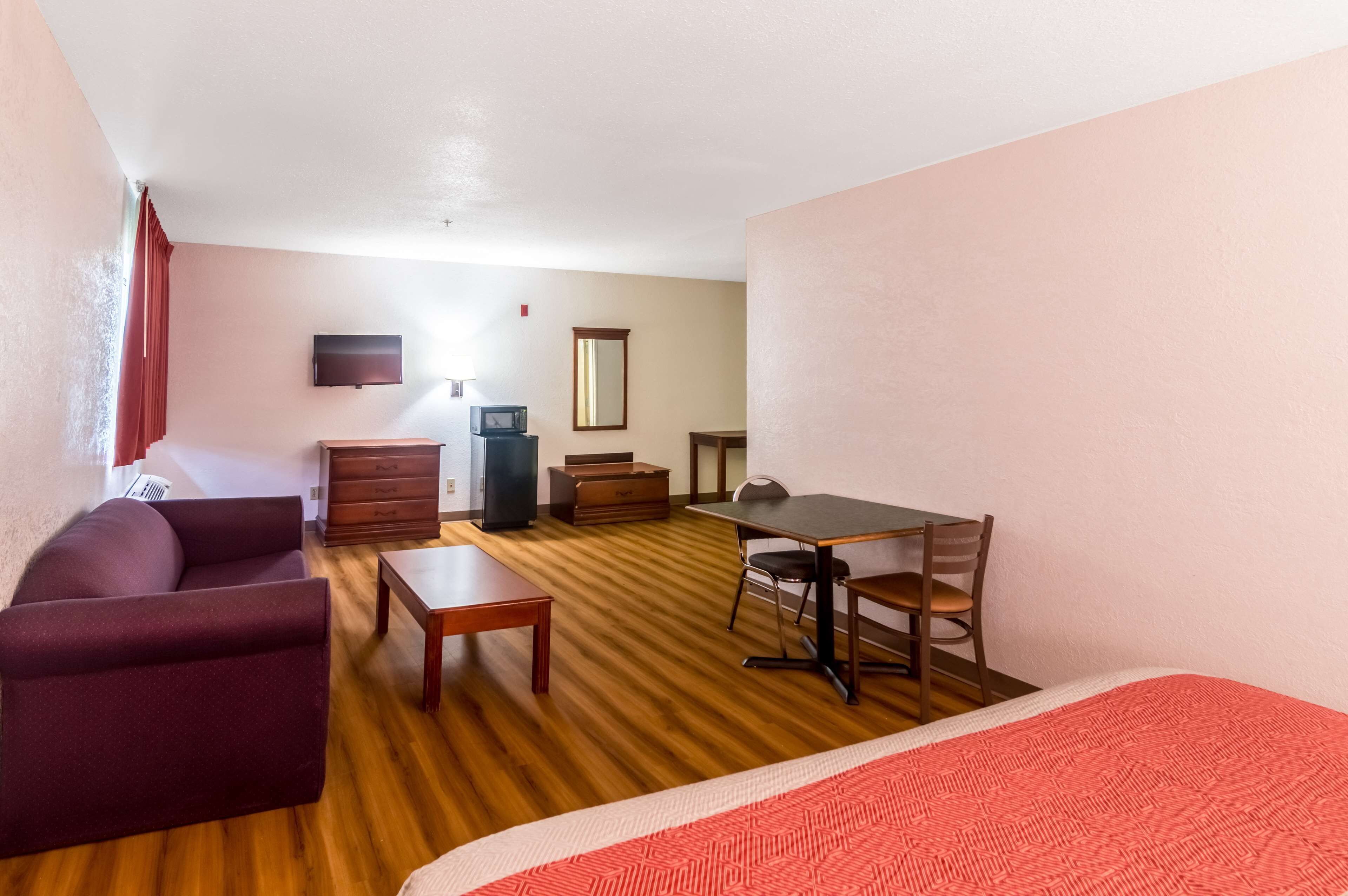 A compact room with a sofa, a small table, a desk with a chair, a television, and a mirror.