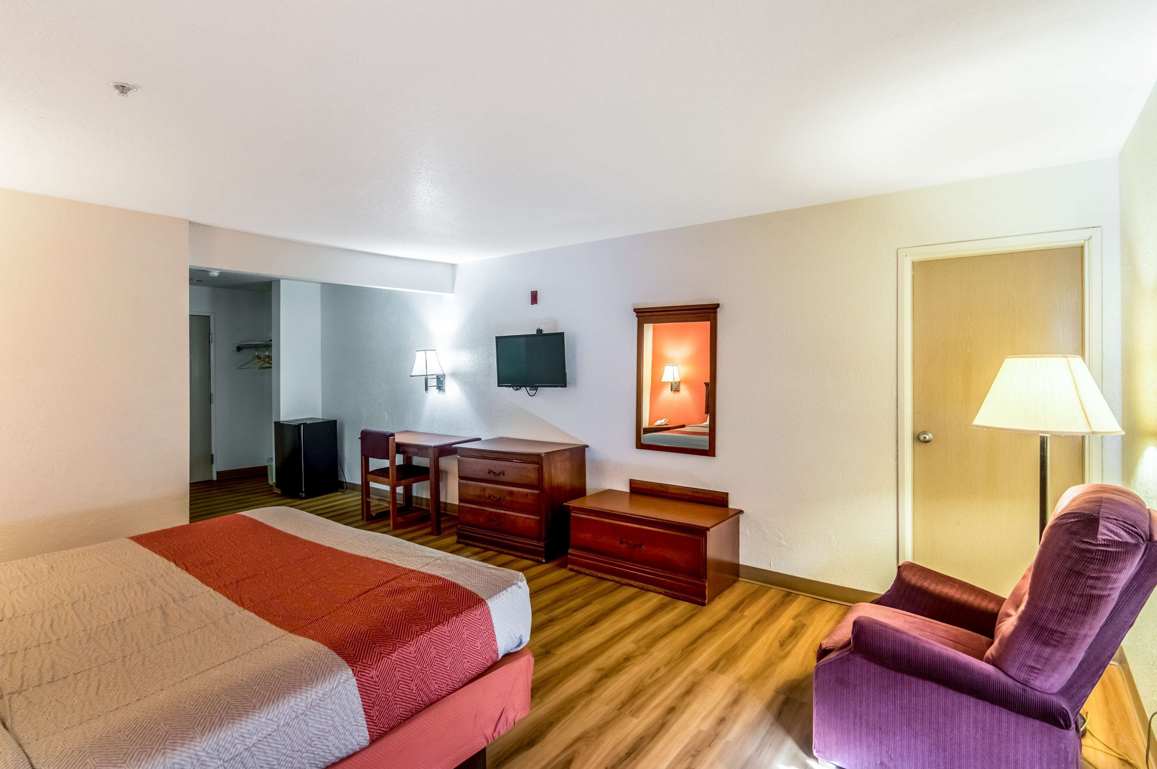 A hotel room with a bed, desk, dresser, chair, and a television.
