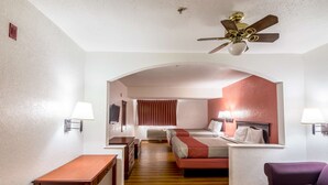 Habitación de hotel con dos camas, un escritorio, una silla, un ventilador de techo y una ventana con cortinas.