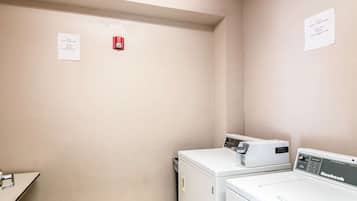 A laundry room with two white washing machines and a red fire alarm.