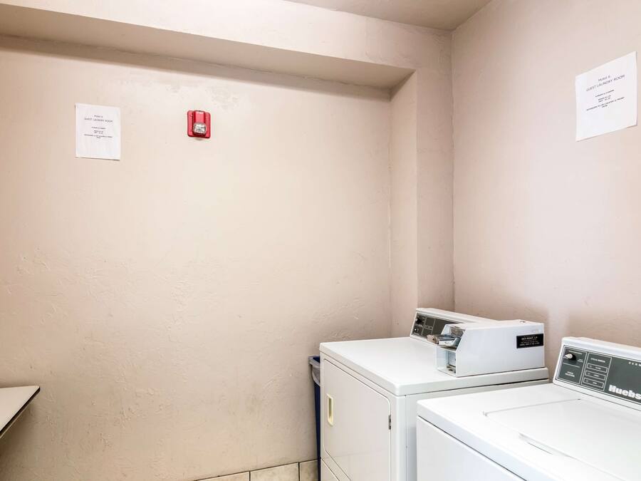 A laundry room with two white washing machines and a red fire alarm.