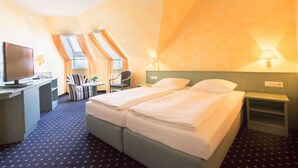 A hotel room with two beds, a desk with a television, a chair, and a small table. - Trip Inn Hotel Astoria Göttingen (Goettingen)