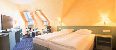 A hotel room with two beds, a desk with a television, a chair, and a small table.