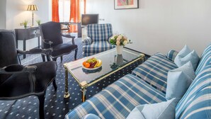 A living room with a blue and white checkered sofa, a glass coffee table with fruit, and a TV in the background. - Trip Inn Hotel Astoria Göttingen (Goettingen)
