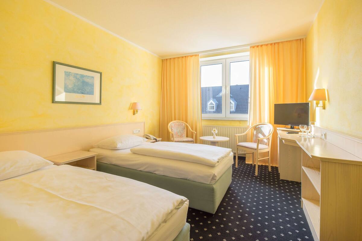 Une chambre d’hôtel avec deux lits, un bureau, une chaise, une télévision et une fenêtre avec des rideaux.