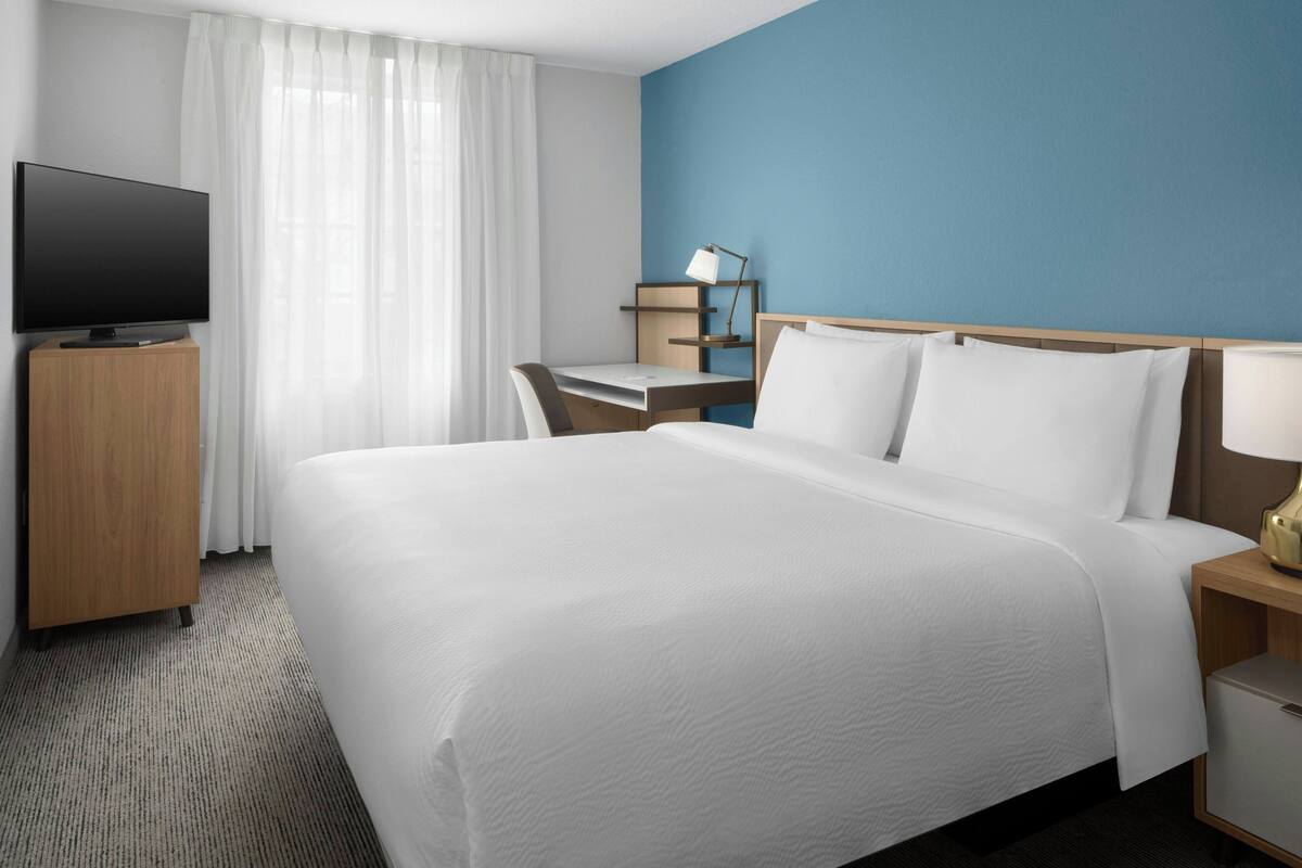 Una habitación de hotel con una cama grande, un escritorio, un televisor y una mesita de noche.