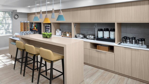 A modern kitchen with a central island, bar stools, hanging pendant lights, and built-in appliances.