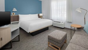 A hotel room with a bed, a TV, a desk, a chair, a sofa, a lamp, and a window with curtains.