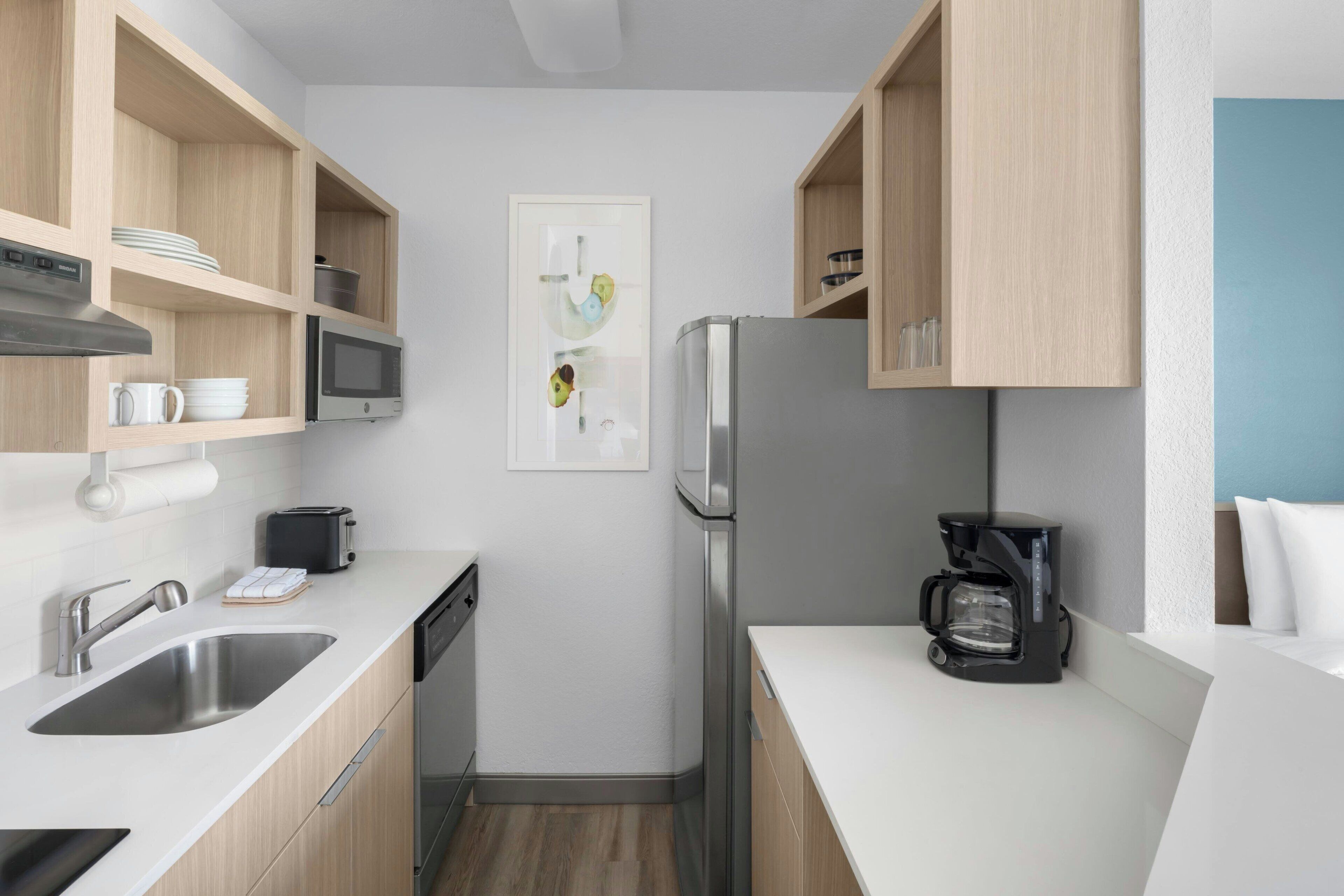 A modern kitchen with a stainless steel refrigerator, a coffee maker, and wooden cabinets.