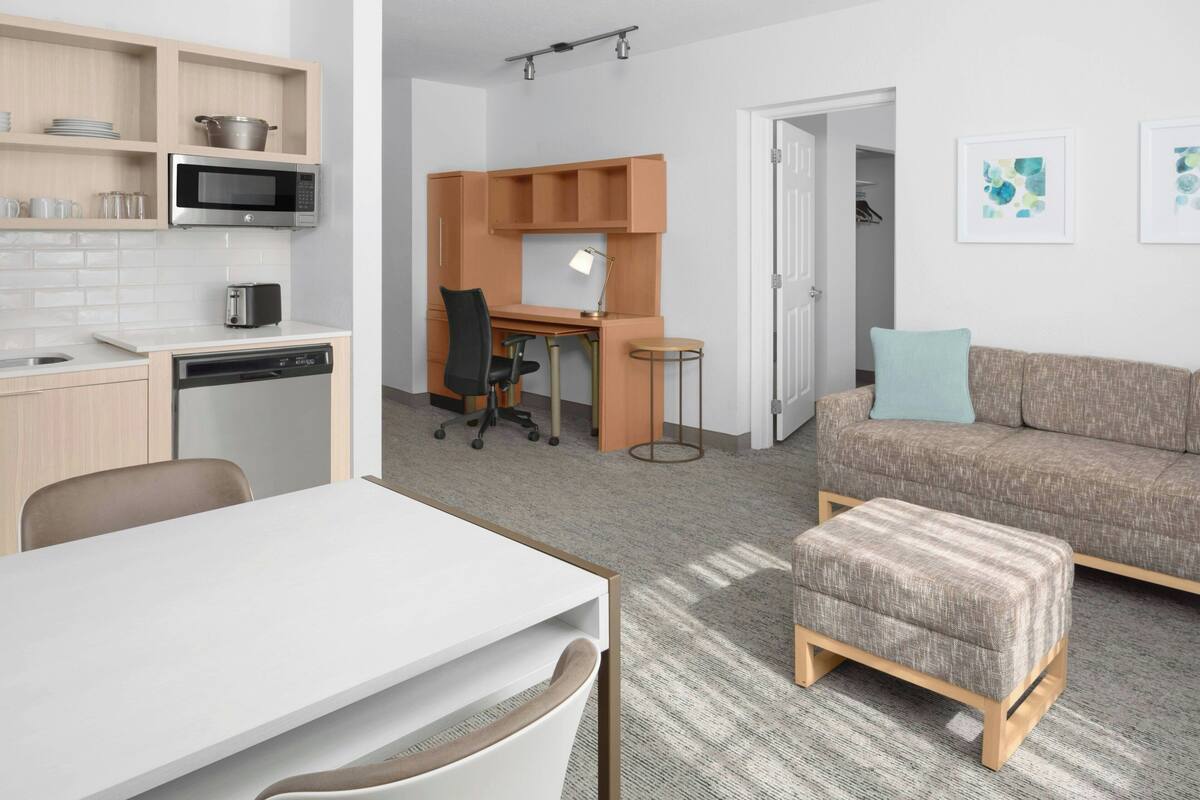 Un apartamento moderno con kitchenette, comedor, espacio de trabajo y sala de estar con sofá y reposapiés.