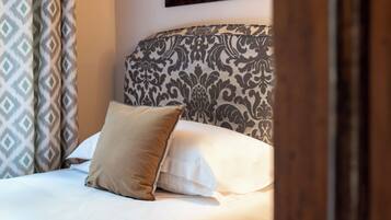 Un letto rifatto con cura, una testiera a fantasia, un cuscino beige e uno bianco.