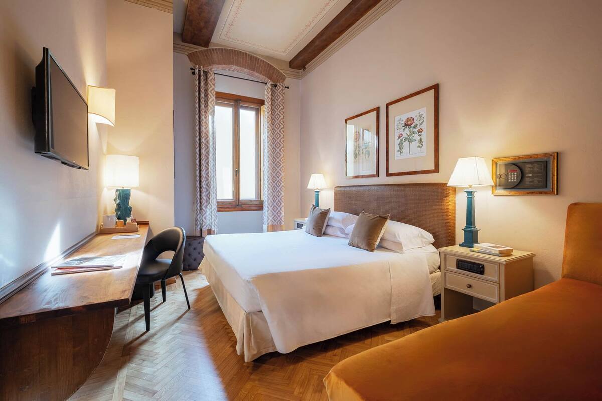 A hotel room with a bed, bedside tables, a desk, a chair, and a TV.