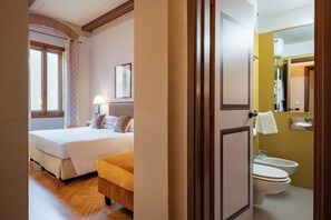 A hotel room with a bed, a bedside table with a lamp, a window with curtains, and a bathroom with a toilet and bidet. - Guest House Morandi (Florence)