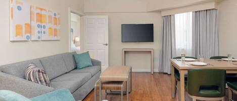 A modern living room with a grey sofa, a small table, and a dining area with a table and chairs.