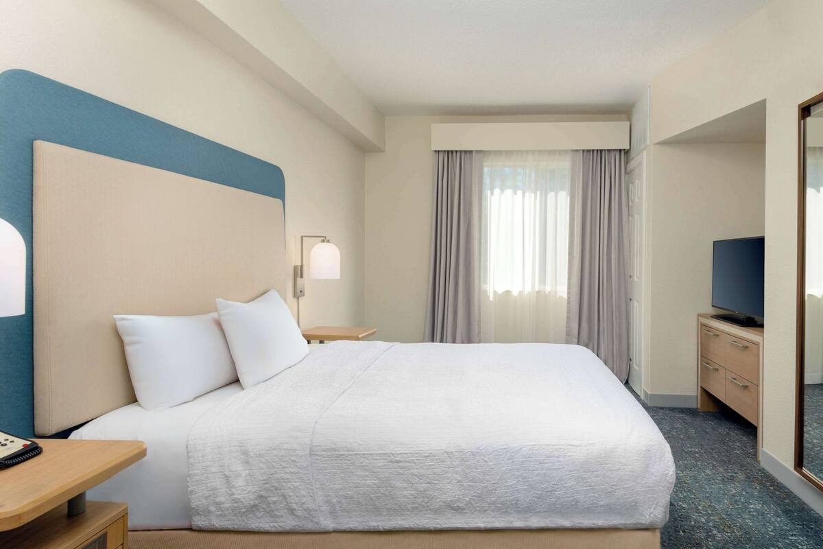 Ein Hotelzimmer mit einem großen Bett, einem Nachttisch mit Lampe, einem Fernseher und einem Kleiderschrank.