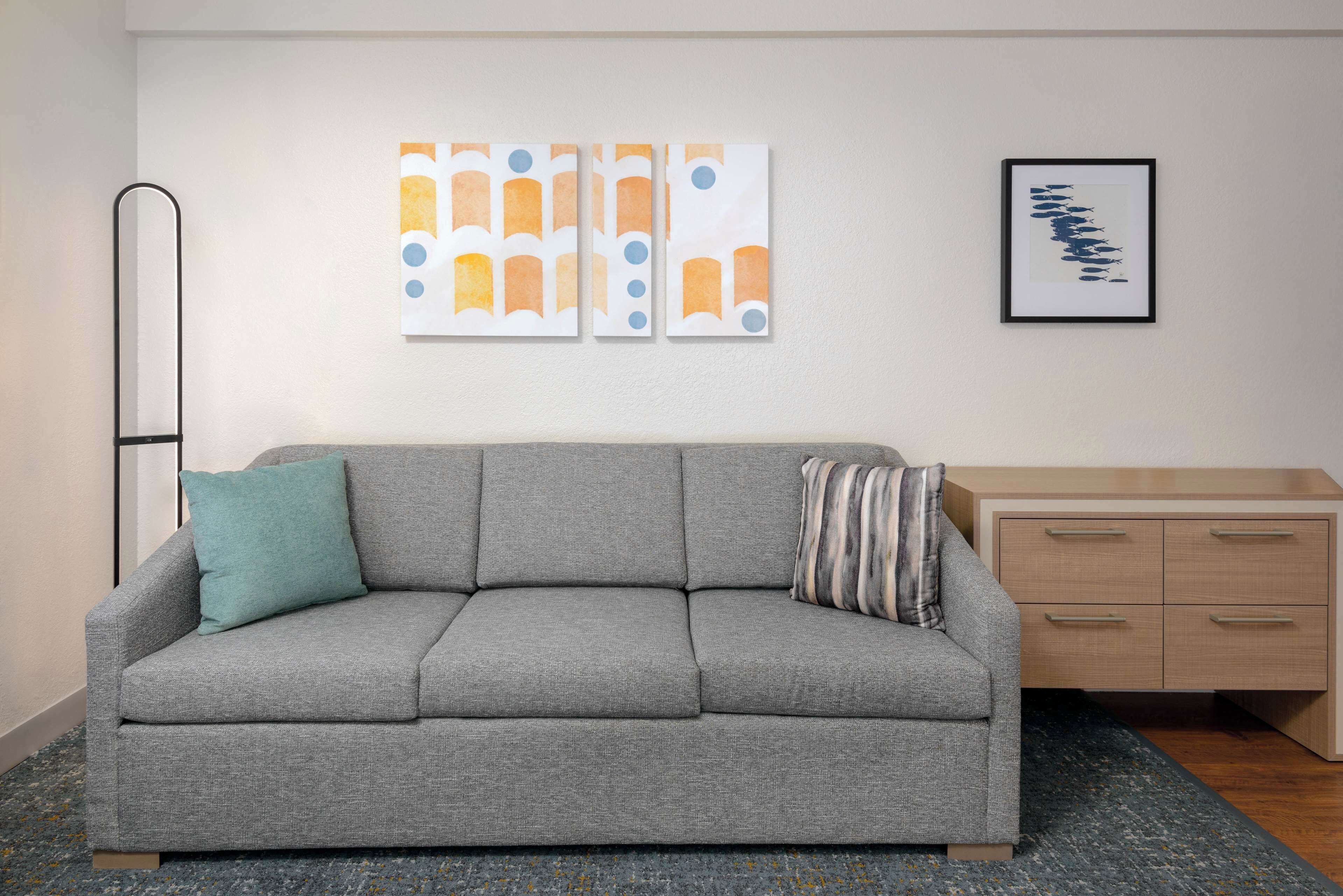 Ein graues Sofa mit türkisfarbenen und gestreiften Kissen, ein Holznachttisch und abstrakte Kunst an der Wand.