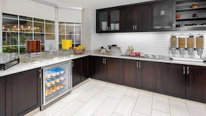 A modern kitchen with dark wood cabinets, a built-in refrigerator, and a window overlooking a garden. - Homewood Suites by Hilton Bonita Springs Naples North (Bonita Springs)