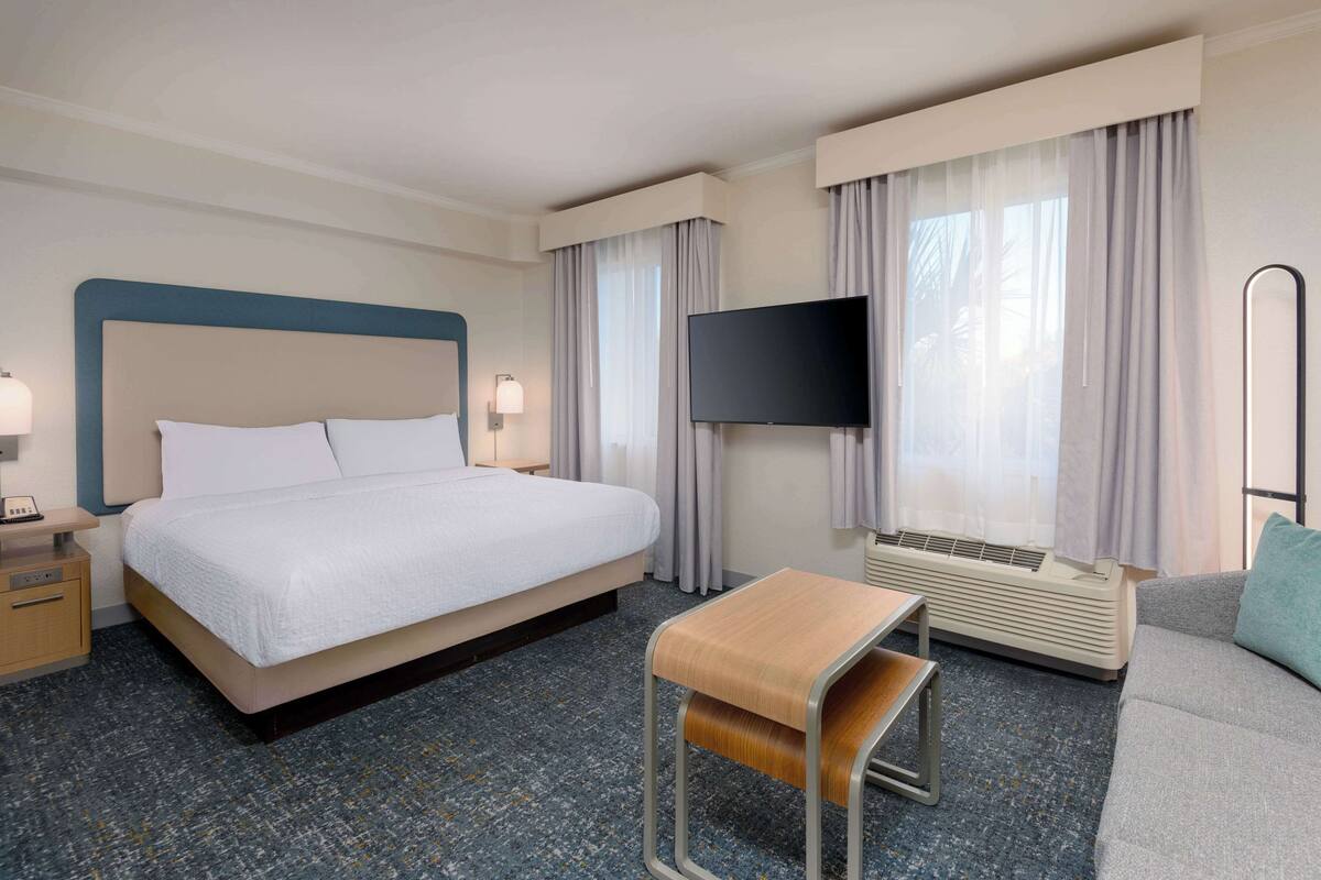Ein Hotelzimmer mit Bett, Nachttisch, Lampe, Fernseher, Klimaanlage und einem kleinen Tisch.