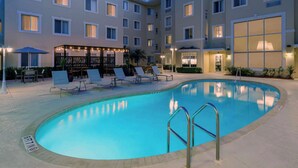 A swimming pool with lounge chairs and umbrellas, surrounded by a multi-story hotel building with balconies and large windows. - Homewood Suites by Hilton Bonita Springs Naples North (Bonita Springs)