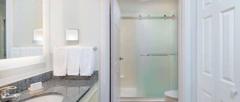 A modern bathroom with a granite countertop sink, a mirror, a towel rack, and a glass-enclosed shower.