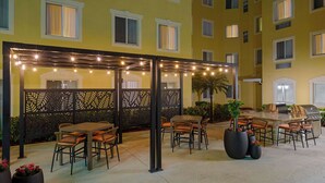 An outdoor patio area with tables and chairs, a grill station, and a decorative fence. - Homewood Suites by Hilton Bonita Springs Naples North (Bonita Springs)
