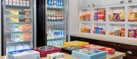 A kitchen with a refrigerator stocked with beverages and snacks, a countertop with various food items, and cabinets above the counter.