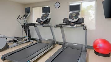 Tres cintas de correr en una sala con un reloj y un televisor en la pared.