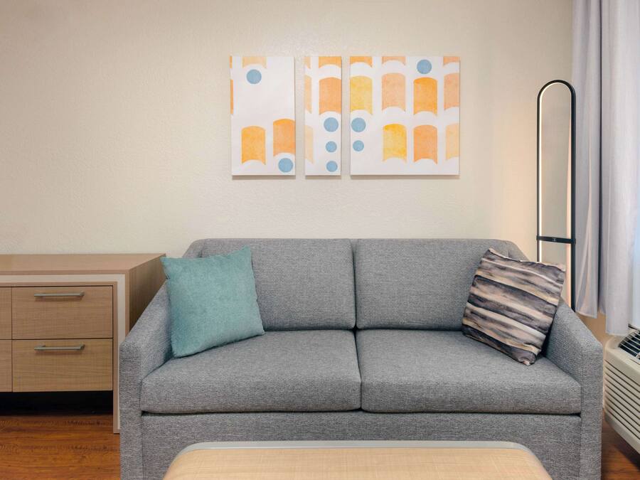 Ein modernes Wohnzimmer mit grauem Sofa, Kissen in Türkis und Streifenoptik, einem Holznachttisch und abstrakter Wandkunst.