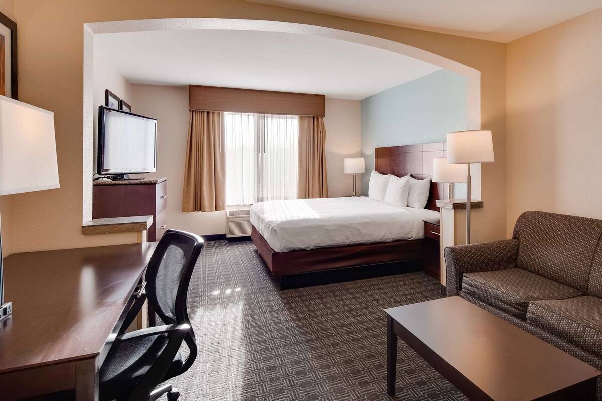 A hotel room with a bed, a desk, a chair, a sofa, and a TV.