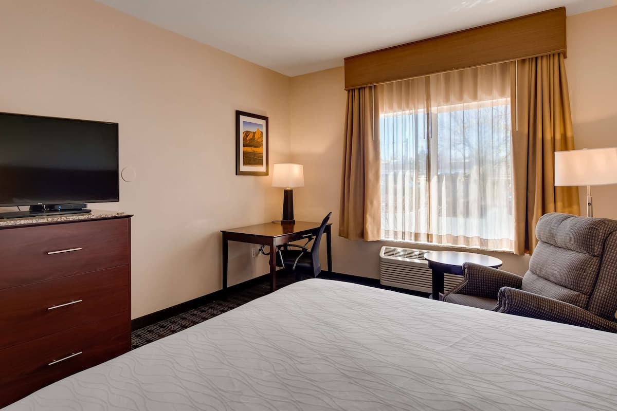 A hotel room with a bed, a desk with a chair, a television, a lamp, and a window with curtains.