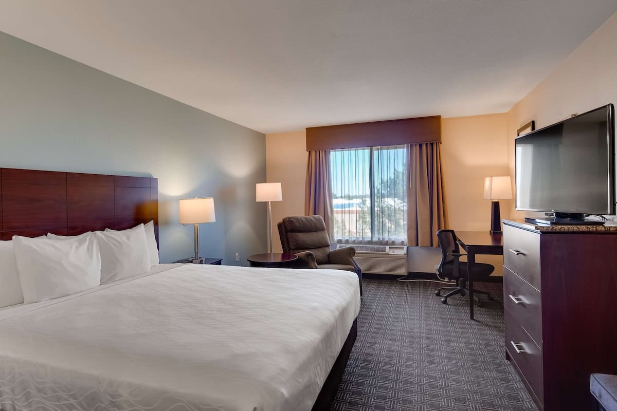 A hotel room with a large bed, a desk with a television, a chair, and a dresser.