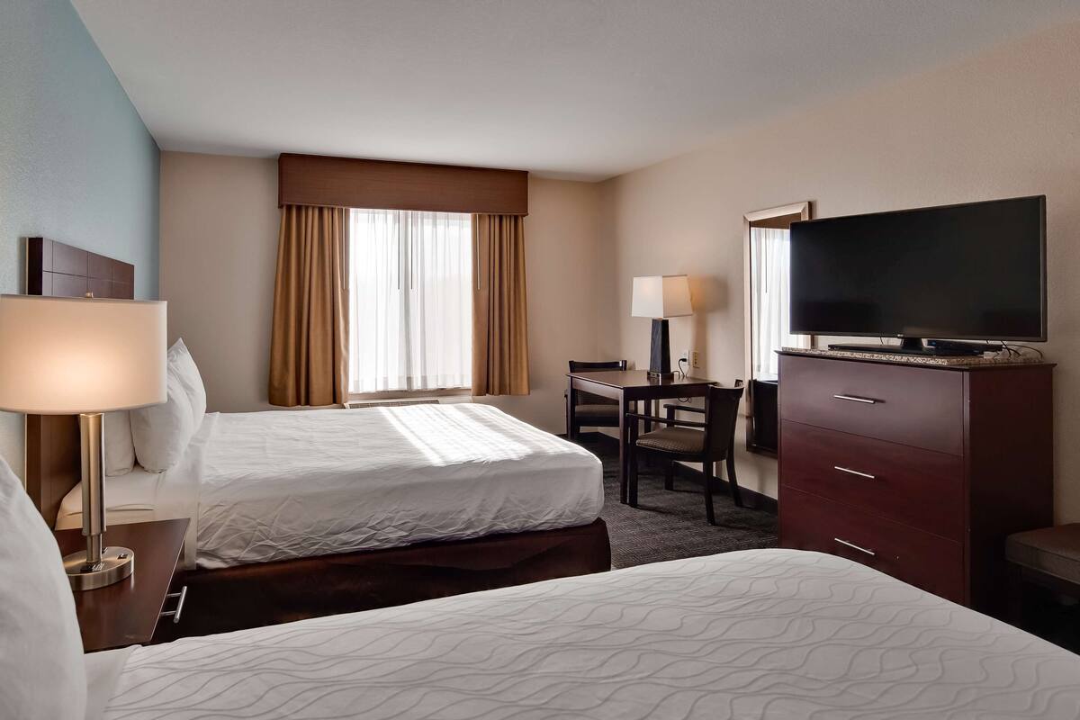 A hotel room with two beds, a desk, a TV, and a dresser.