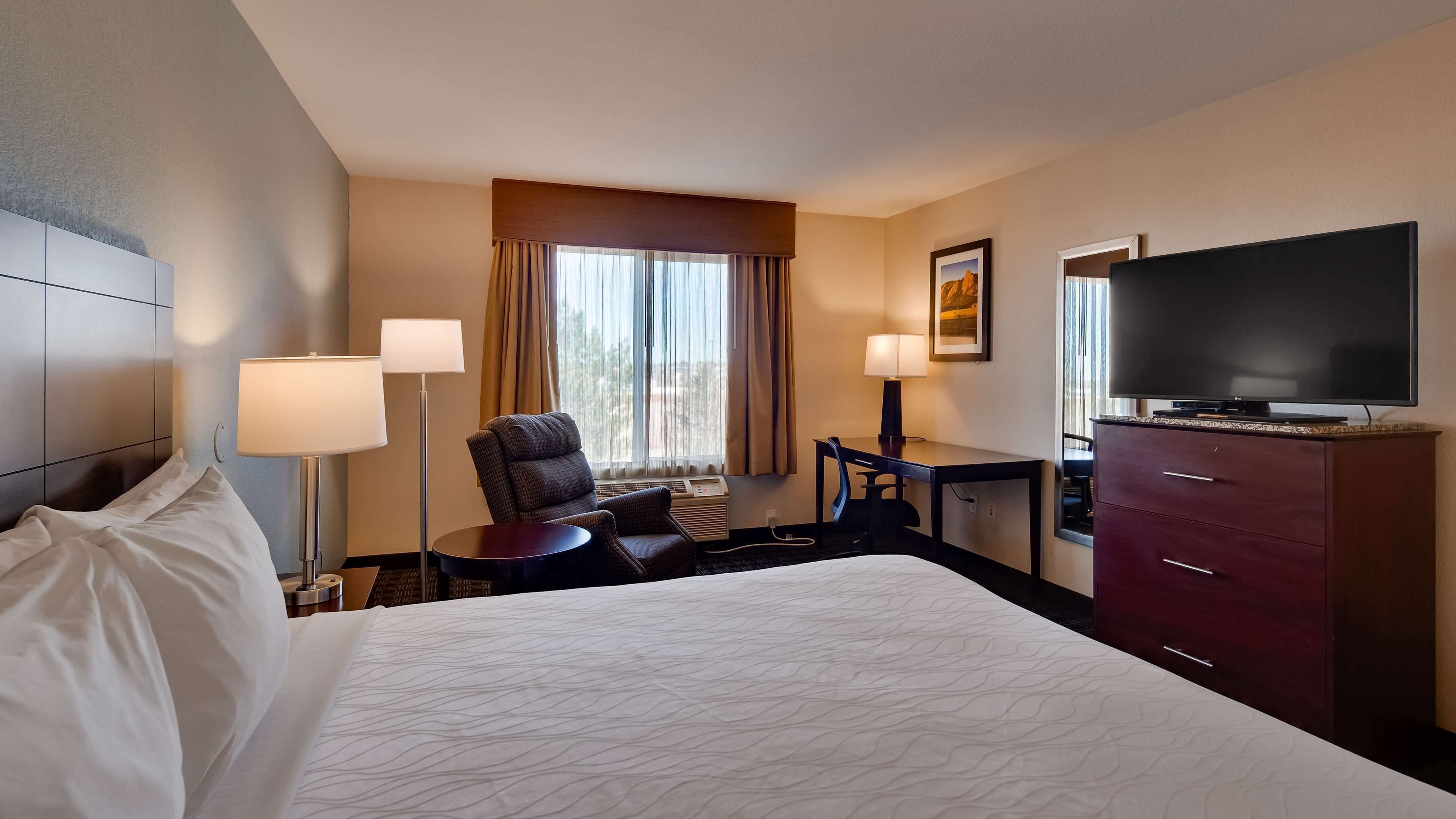 A hotel room with a large bed, a desk, a chair, a TV, and a dresser.