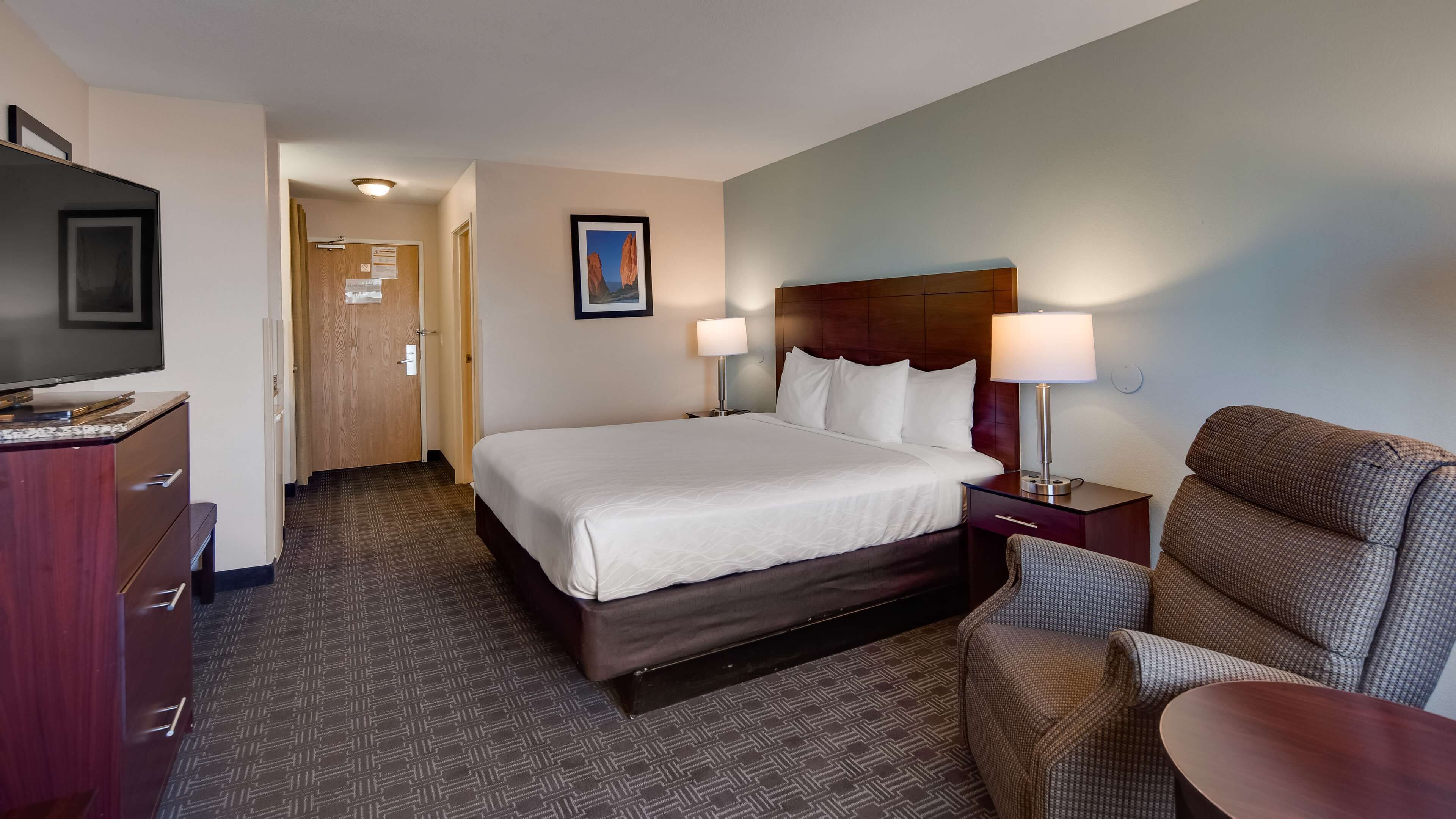 A hotel room with a bed, bedside tables, a TV, a desk, and a chair.