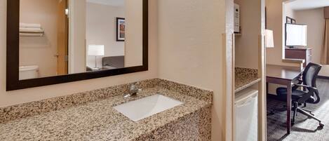 Baño de hotel con lavamanos de encimera de granito, un espejo grande y un inodoro que se ve en el reflejo.