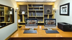 Una sala de conferencias con dos ordenadores de escritorio, una impresora y una estantería con objetos decorativos.