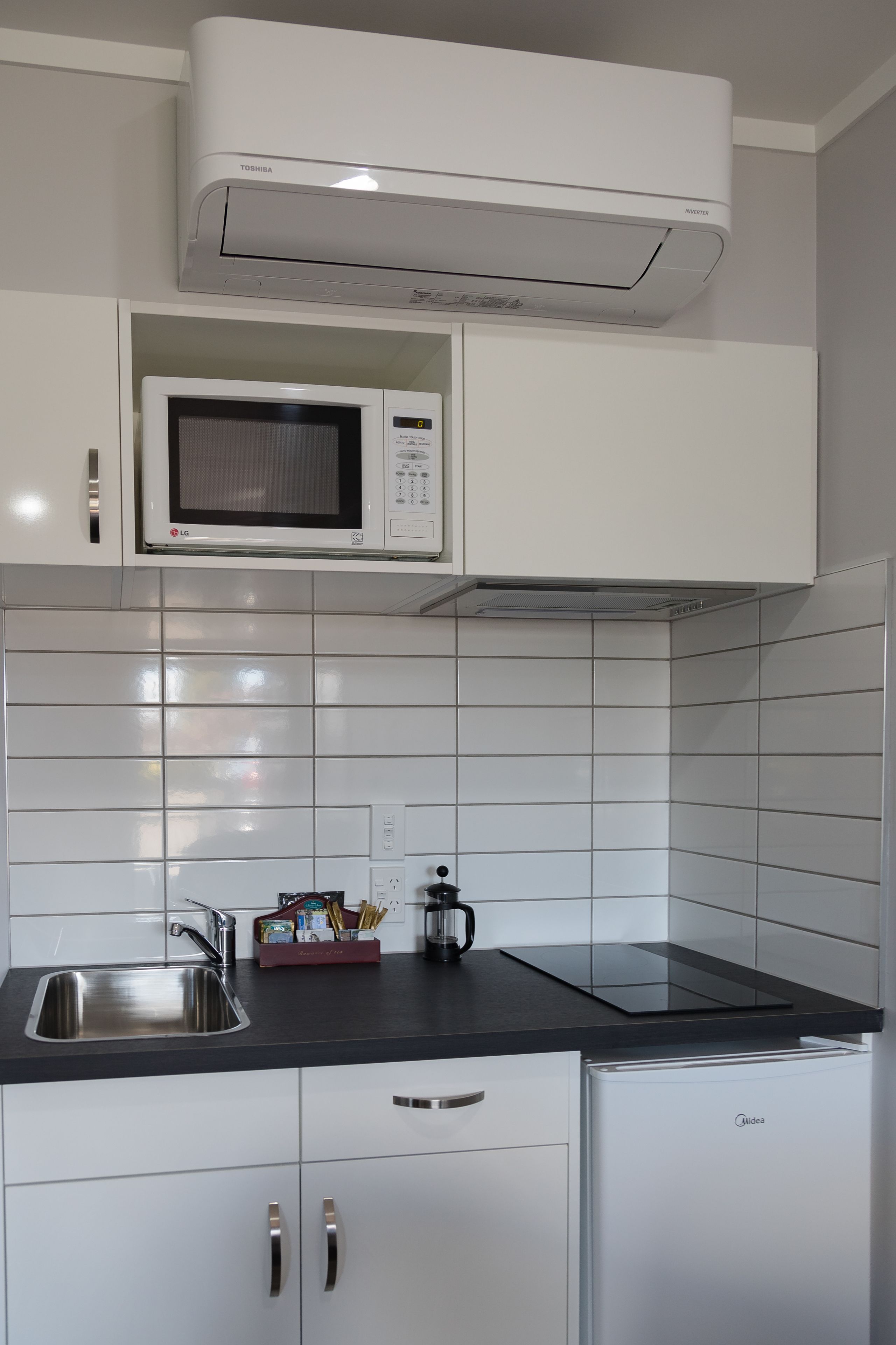A modern kitchen with white cabinets, a stainless steel sink, a microwave, and a compact refrigerator.