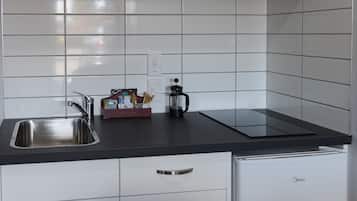A modern kitchen with white cabinets, a stainless steel sink, a microwave, and a compact refrigerator.