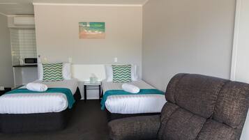 A hotel room with two beds, a gray armchair, a small table with a lamp, and a painting on the wall.