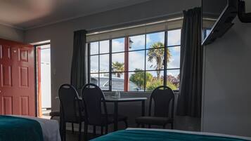 A hotel room with a bed, a desk, two chairs, and a window with a view of palm trees and a car outside.