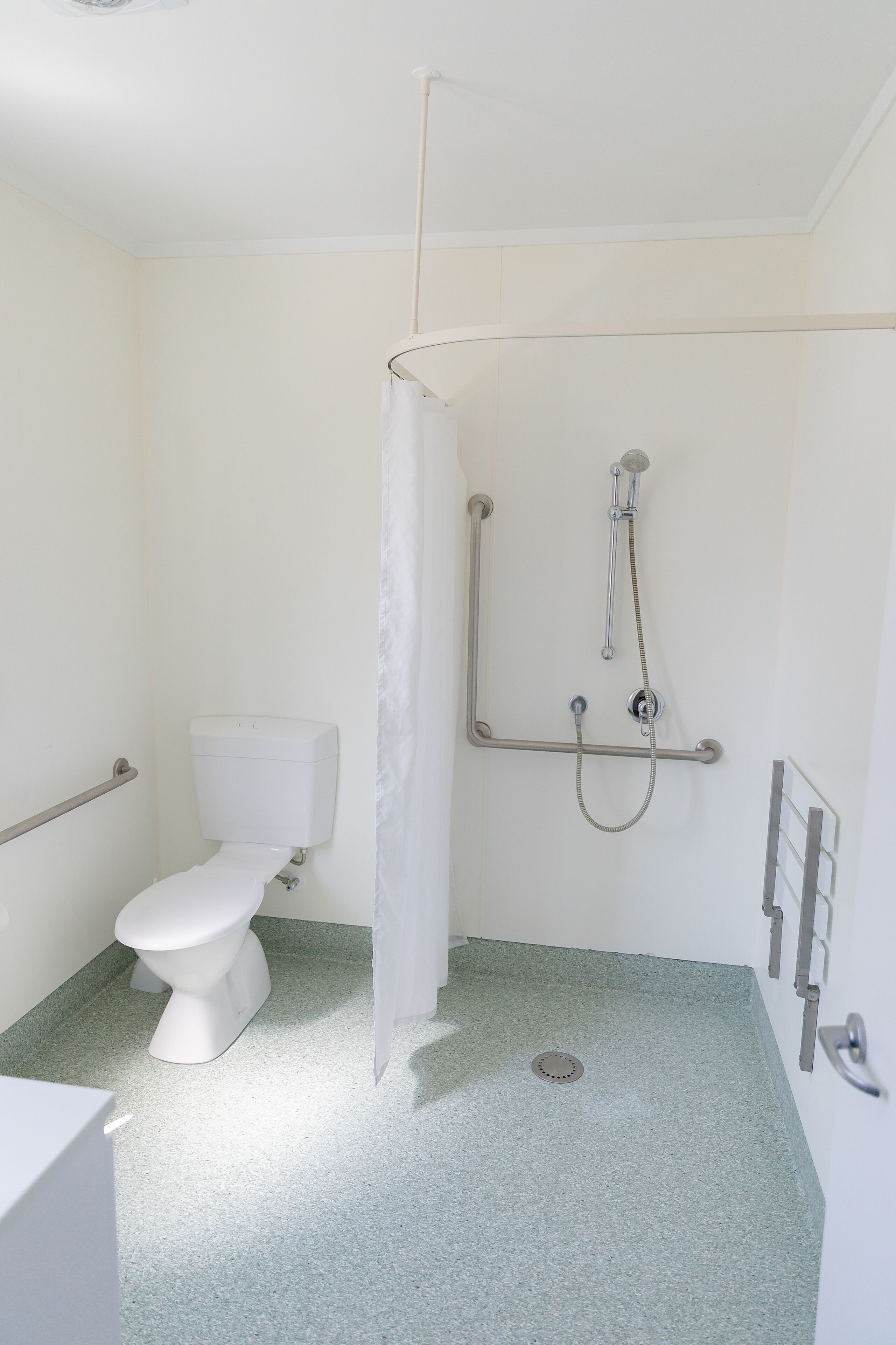 A bathroom with a toilet, a shower with a grab bar, and a floor drain.