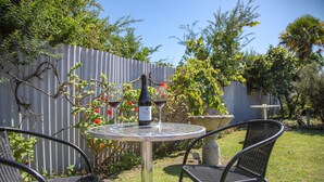 A patio with a round table and two chairs, a bottle of wine, and a fence with climbing plants. - Bk's Palm Court Motor Lodge (Gisborne)